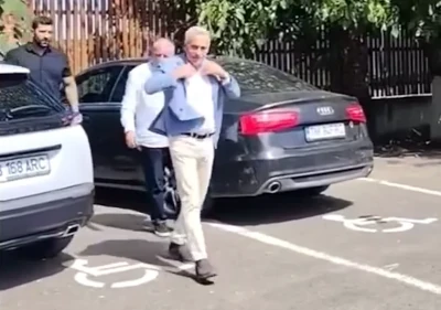 Călin Georgescu devant sa voiture garée à cheval sur deux places de stationnement réservé